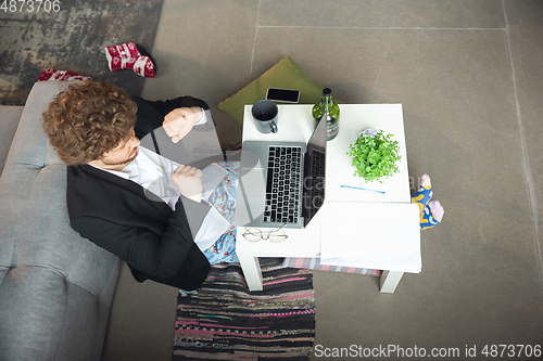 Image of Young man without pants but in jacket working on a computer, laptop. Remote office during coronavirus, fun and comfortable work in underpants