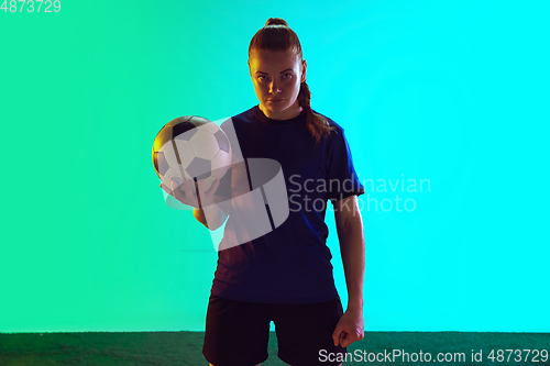 Image of Female soccer, football player holding ball, posing confident isolated on gradient background. Copyspace.