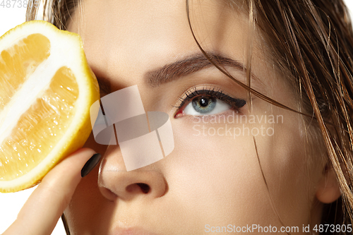 Image of Close up of beautiful young woman with lemon slices over white background. Cosmetics and makeup, natural and eco treatment, skin care.