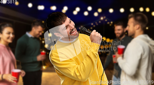 Image of man with microphone singing at night rooftop party