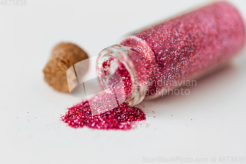 Image of pink red glitters poured from small glass bottle