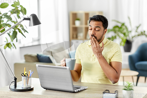 Image of man with laptop and coffee yawning at home office