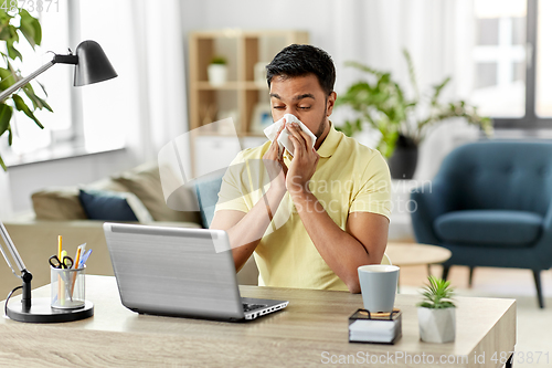 Image of indian man with laptop blowing nose at home office