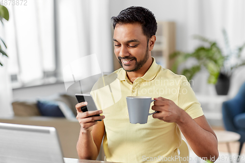 Image of man with smartphone drinking coffee at home office