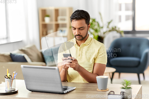 Image of happy indian man with smartphone at home office