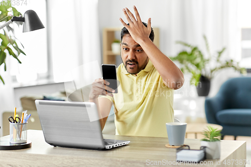 Image of angry indian man with smartphone at home office