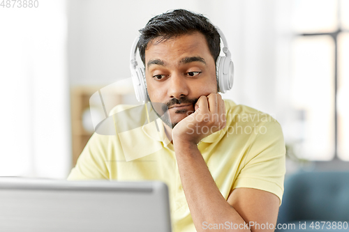 Image of bored man in headphones with laptop works at home