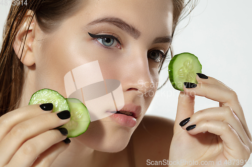 Image of Close up of beautiful young woman with cucumber slices over white background. Cosmetics and makeup, natural and eco treatment, skin care.