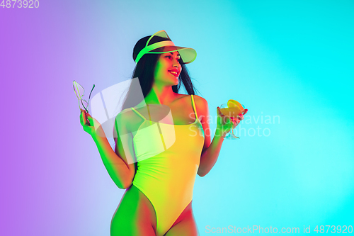 Image of Beautiful girl in fashionable swimsuit isolated on gradient studio background in neon light. Summer, resort, fashion and weekend concept