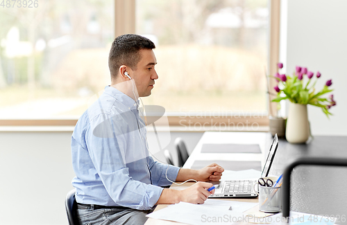 Image of man in earphones with laptop working at home