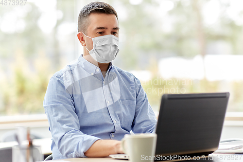 Image of man in mask with laptop working at home office