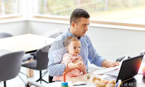 Image of father with baby working on laptop at home office