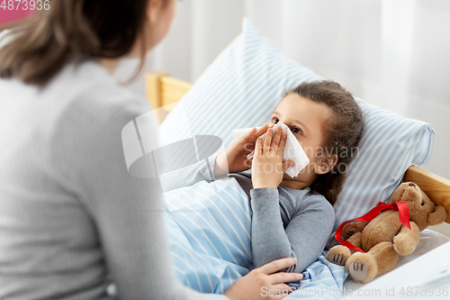 Image of mother and ill little daughter blowing nose in bed