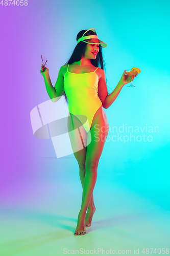 Image of Beautiful girl in fashionable swimsuit isolated on gradient studio background in neon light. Summer, resort, fashion and weekend concept