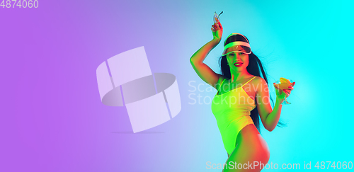 Image of Beautiful girl in fashionable swimsuit isolated on gradient studio background in neon light. Summer, resort, fashion and weekend concept. Flyer with copyspace.