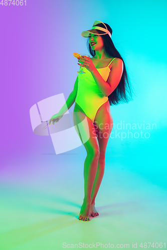 Image of Beautiful girl in fashionable swimsuit isolated on gradient studio background in neon light. Summer, resort, fashion and weekend concept