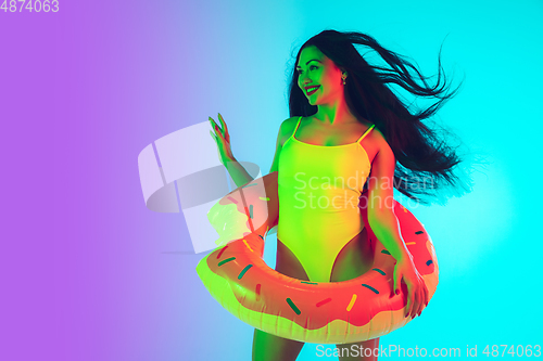 Image of Beautiful girl in fashionable swimsuit isolated on gradient studio background in neon light. Summer, resort, fashion and weekend concept