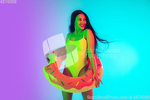 Image of Beautiful girl in fashionable swimsuit isolated on gradient studio background in neon light. Summer, resort, fashion and weekend concept