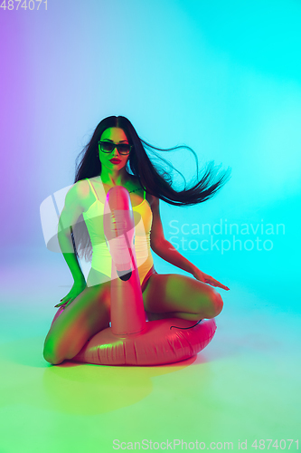 Image of Beautiful girl in fashionable swimsuit isolated on gradient studio background in neon light. Summer, resort, fashion and weekend concept