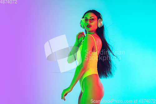 Image of Beautiful girl in fashionable swimsuit isolated on gradient studio background in neon light. Summer, resort, fashion and weekend concept