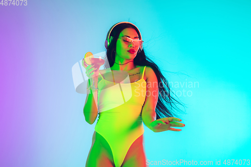 Image of Beautiful girl in fashionable swimsuit isolated on gradient studio background in neon light. Summer, resort, fashion and weekend concept