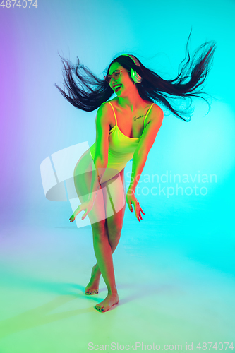 Image of Beautiful girl in fashionable swimsuit isolated on gradient studio background in neon light. Summer, resort, fashion and weekend concept