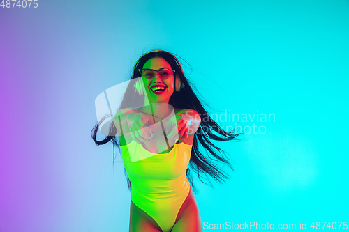 Image of Beautiful girl in fashionable swimsuit isolated on gradient studio background in neon light. Summer, resort, fashion and weekend concept