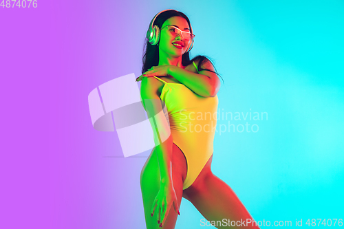 Image of Beautiful girl in fashionable swimsuit isolated on gradient studio background in neon light. Summer, resort, fashion and weekend concept