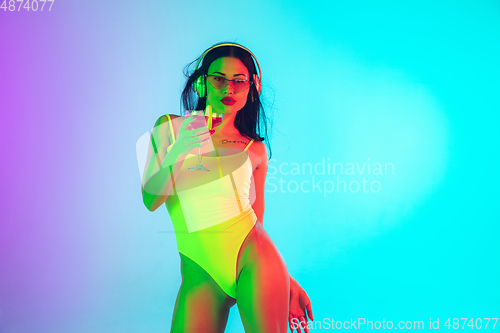 Image of Beautiful girl in fashionable swimsuit isolated on gradient studio background in neon light. Summer, resort, fashion and weekend concept
