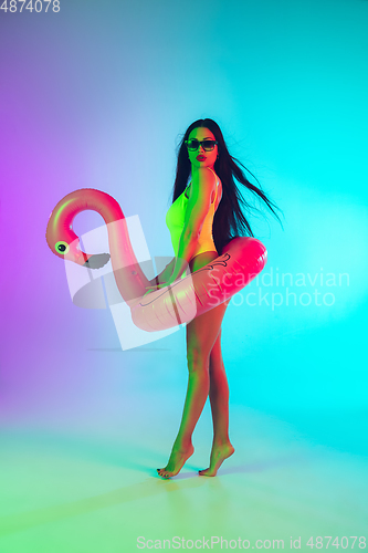 Image of Beautiful girl in fashionable swimsuit isolated on gradient studio background in neon light. Summer, resort, fashion and weekend concept