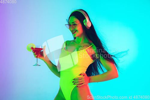 Image of Beautiful girl in fashionable swimsuit isolated on gradient studio background in neon light. Summer, resort, fashion and weekend concept