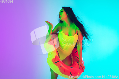 Image of Beautiful girl in fashionable swimsuit isolated on gradient studio background in neon light. Summer, resort, fashion and weekend concept