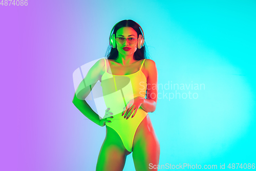 Image of Beautiful girl in fashionable swimsuit isolated on gradient studio background in neon light. Summer, resort, fashion and weekend concept