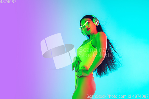 Image of Beautiful girl in fashionable swimsuit isolated on gradient studio background in neon light. Summer, resort, fashion and weekend concept