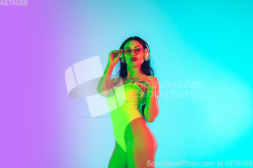 Image of Beautiful girl in fashionable swimsuit isolated on gradient studio background in neon light. Summer, resort, fashion and weekend concept