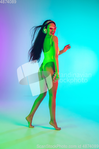 Image of Beautiful girl in fashionable swimsuit isolated on gradient studio background in neon light. Summer, resort, fashion and weekend concept