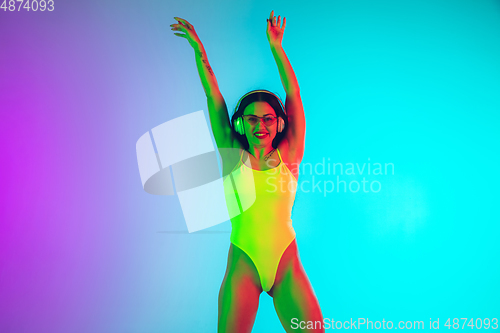 Image of Beautiful girl in fashionable swimsuit isolated on gradient studio background in neon light. Summer, resort, fashion and weekend concept