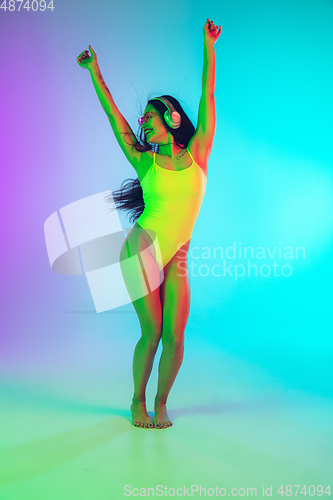 Image of Beautiful girl in fashionable swimsuit isolated on gradient studio background in neon light. Summer, resort, fashion and weekend concept