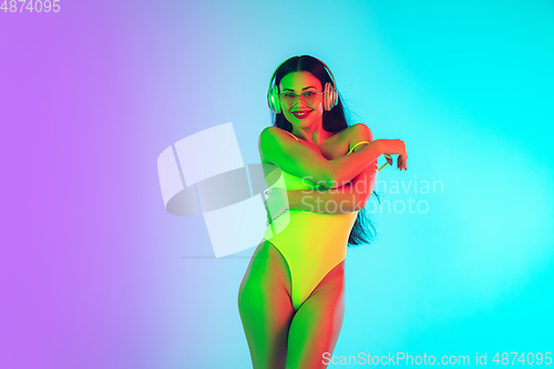 Image of Beautiful girl in fashionable swimsuit isolated on gradient studio background in neon light. Summer, resort, fashion and weekend concept