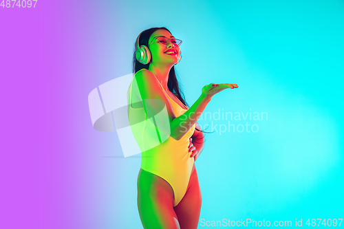 Image of Beautiful girl in fashionable swimsuit isolated on gradient studio background in neon light. Summer, resort, fashion and weekend concept