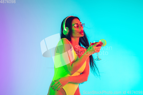 Image of Beautiful girl in fashionable swimsuit isolated on gradient studio background in neon light. Summer, resort, fashion and weekend concept