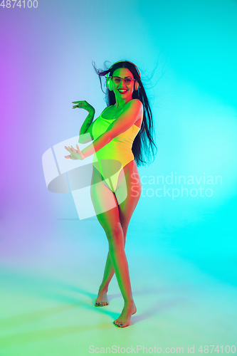 Image of Beautiful girl in fashionable swimsuit isolated on gradient studio background in neon light. Summer, resort, fashion and weekend concept