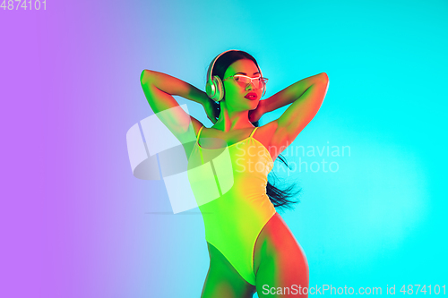 Image of Beautiful girl in fashionable swimsuit isolated on gradient studio background in neon light. Summer, resort, fashion and weekend concept