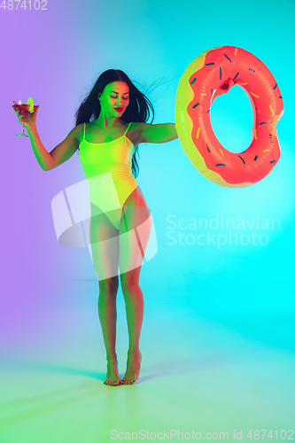 Image of Beautiful girl in fashionable swimsuit isolated on gradient studio background in neon light. Summer, resort, fashion and weekend concept