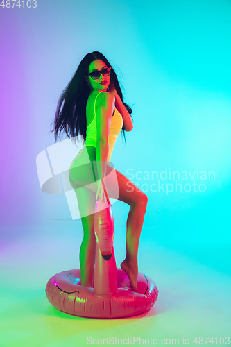 Image of Beautiful girl in fashionable swimsuit isolated on gradient studio background in neon light. Summer, resort, fashion and weekend concept