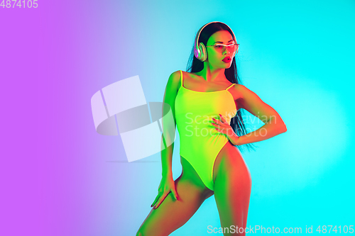 Image of Beautiful girl in fashionable swimsuit isolated on gradient studio background in neon light. Summer, resort, fashion and weekend concept