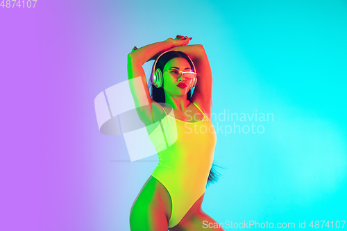 Image of Beautiful girl in fashionable swimsuit isolated on gradient studio background in neon light. Summer, resort, fashion and weekend concept