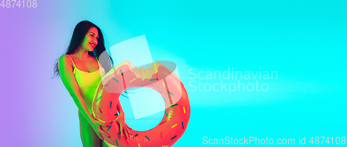 Image of Beautiful girl in fashionable swimsuit isolated on gradient studio background in neon light. Summer, resort, fashion and weekend concept. Flyer with copyspace.