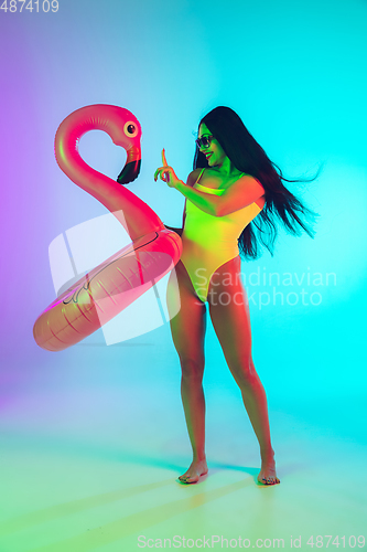 Image of Beautiful girl in fashionable swimsuit isolated on gradient studio background in neon light. Summer, resort, fashion and weekend concept