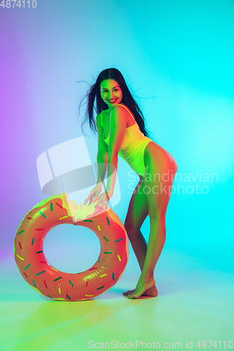 Image of Beautiful girl in fashionable swimsuit isolated on gradient studio background in neon light. Summer, resort, fashion and weekend concept